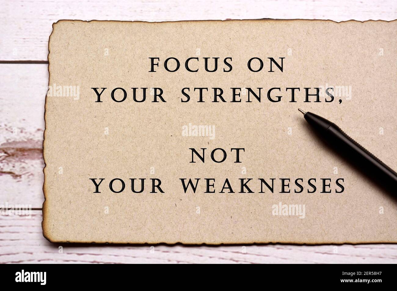 Motivational and inspirational quote on burnt edge brown paper with pen on wooden desk - Focus on your strengths, not your weaknesses Stock Photo