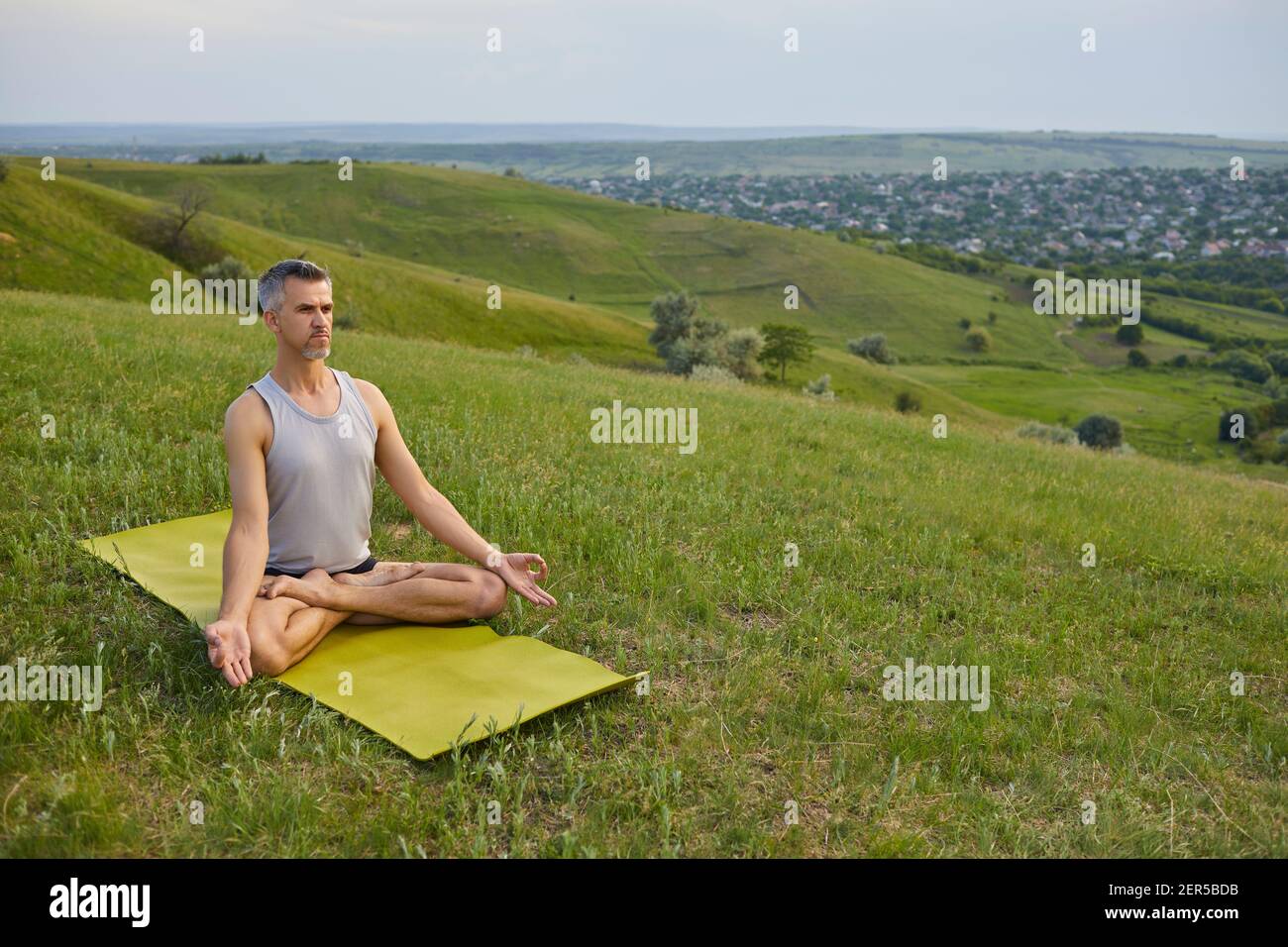 Mature male meditating on grassy hill Stock Photo