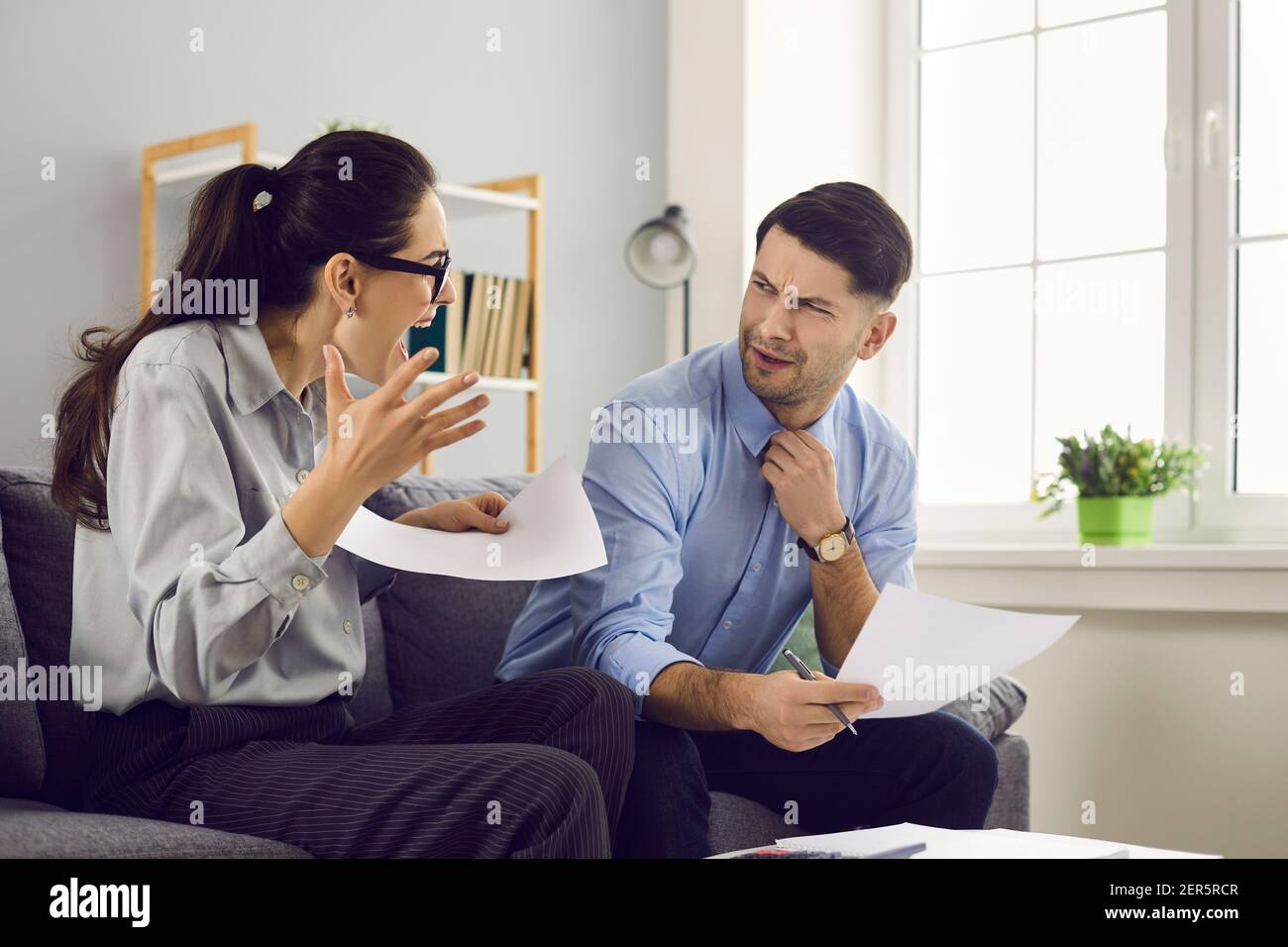 Angry couple sitting on sofa and quarreling over debts, expenses and high utility bills Stock Photo