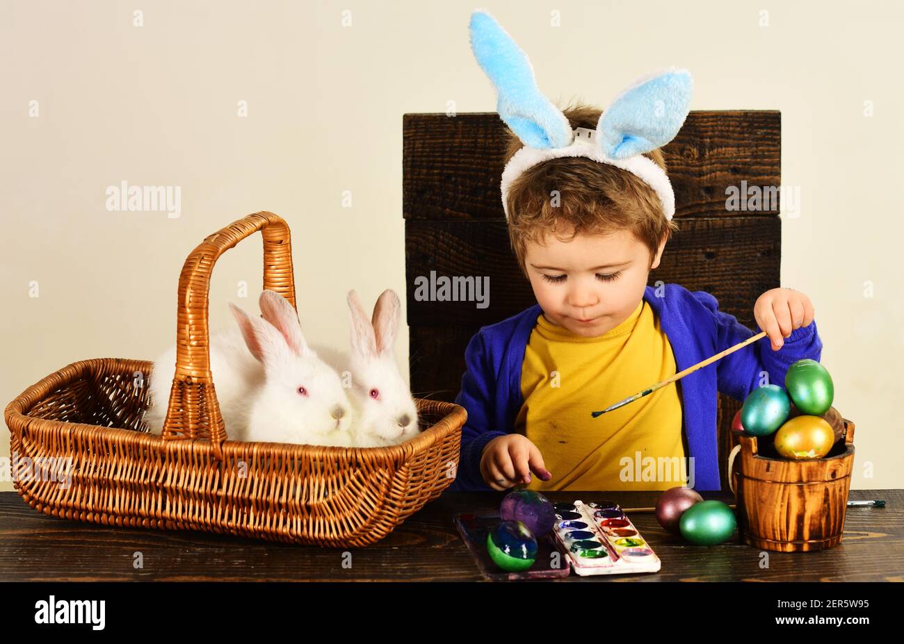 Child in bunny ears paint Easter egg. Little boy with easters rabbit in basket. Stock Photo