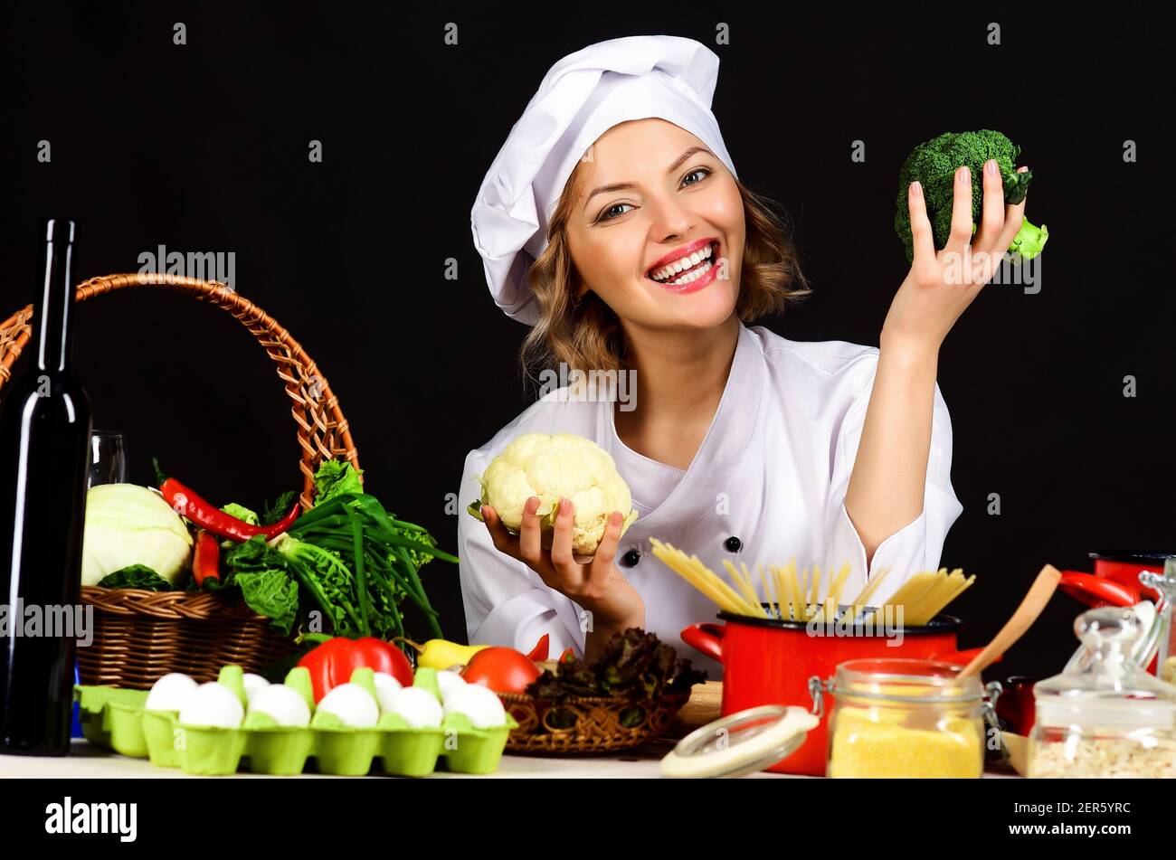 Smiling female chef with broccoli. Healthy food preparation. Cooking in Restaurant. Dieting, vegetarian. Stock Photo