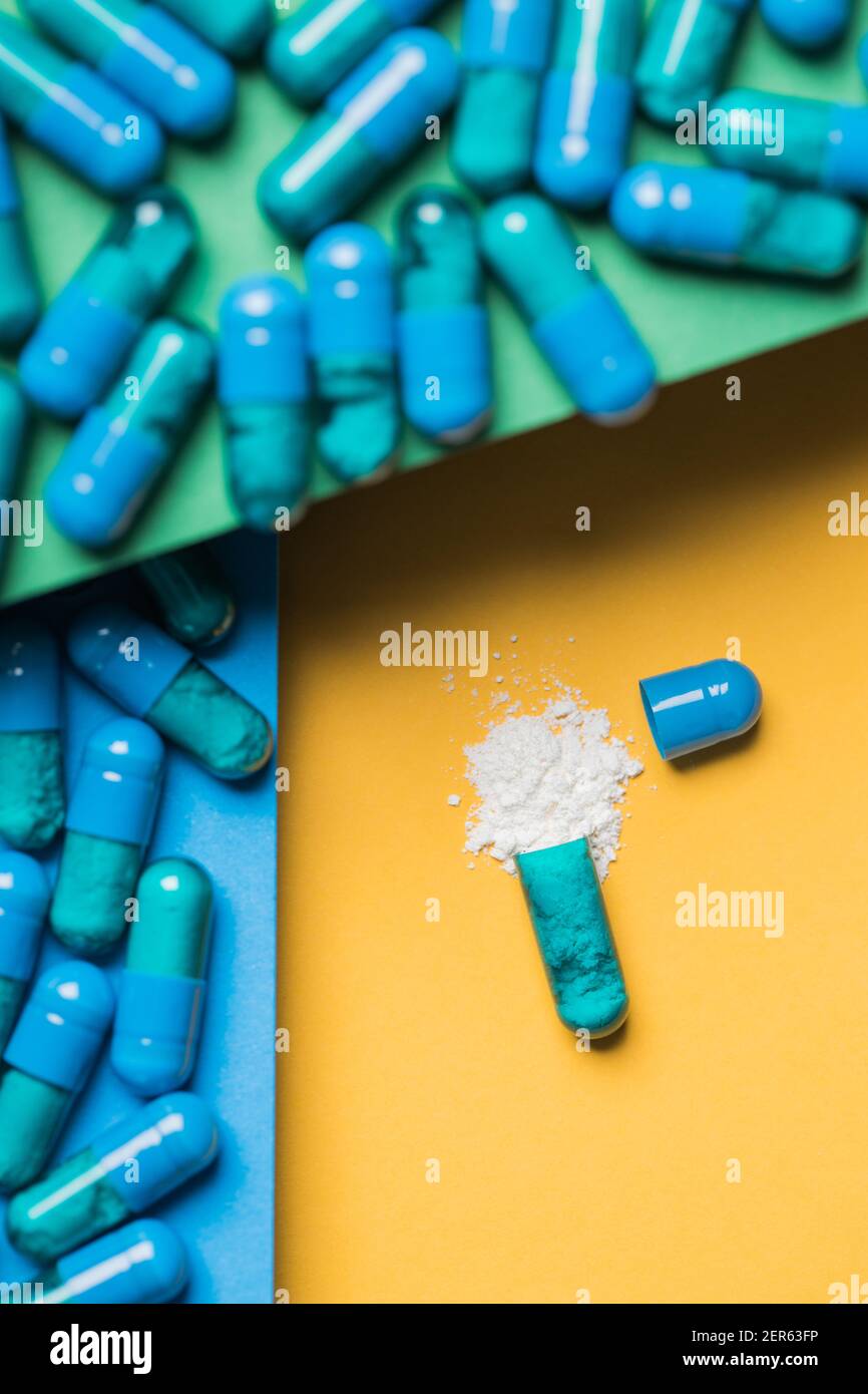 High angle of contents of medical drug poured out of blue colored capsule on yellow background