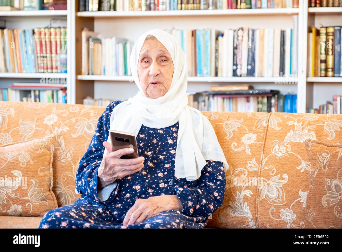 Happy old arabic muslim woamn using technology while sitting on couch Stock Photo