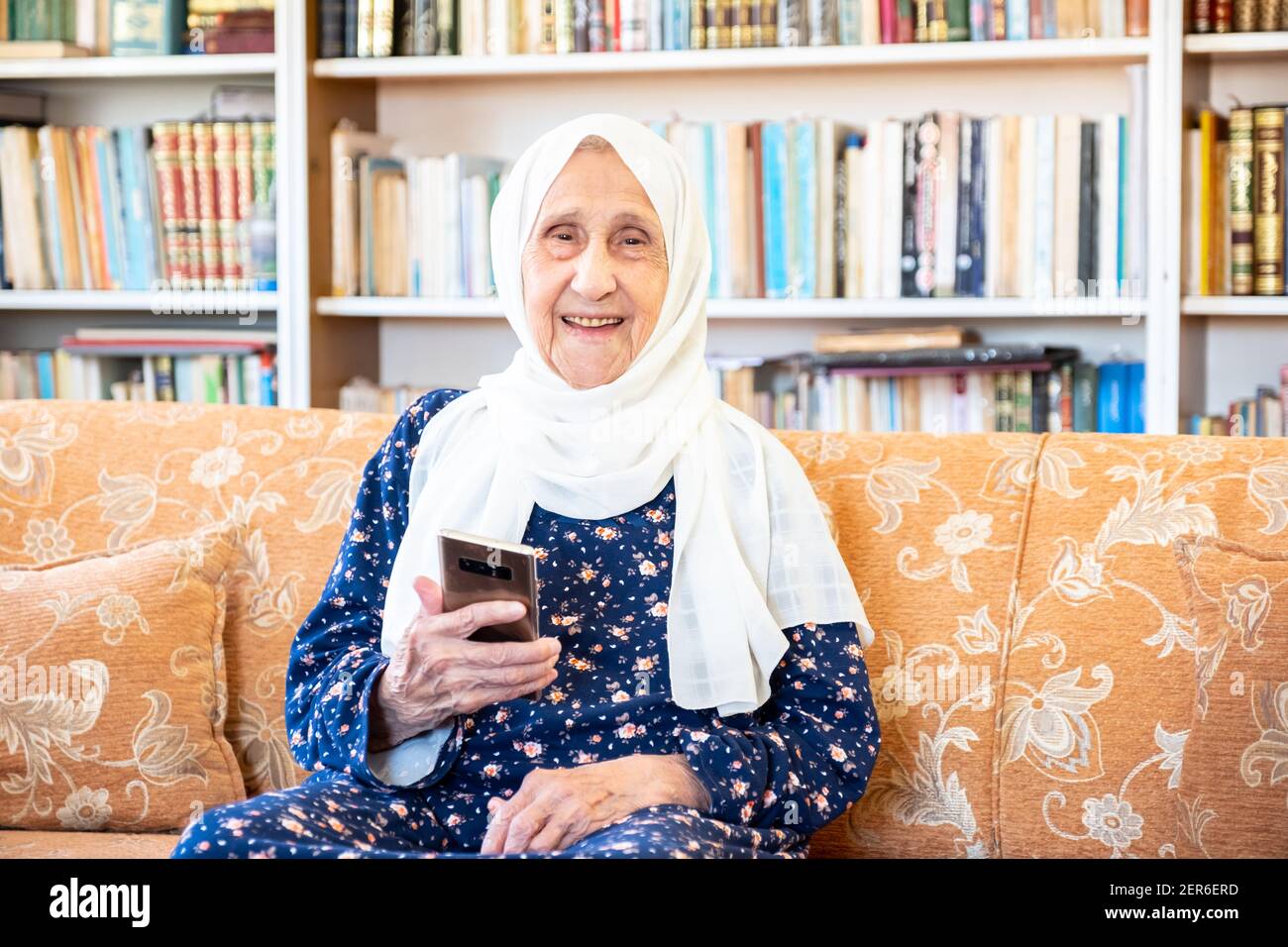 Happy old arabic muslim woamn using technology while sitting on couch Stock Photo