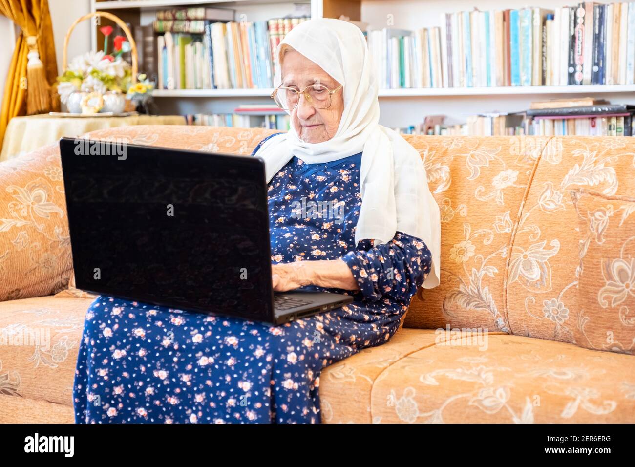 Happy old arabic muslim woamn using technology while sitting on couch Stock Photo