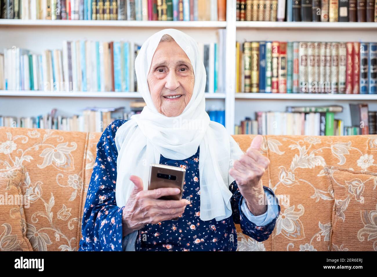 Happy old arabic muslim woamn using technology while sitting on couch Stock Photo