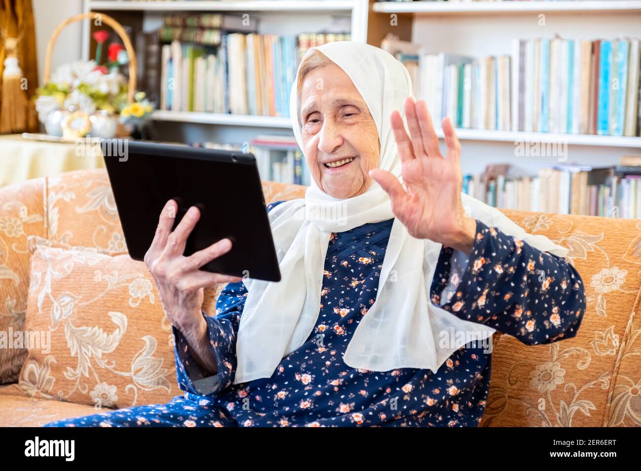 Happy old arabic muslim woamn using technology while sitting on couch Stock Photo