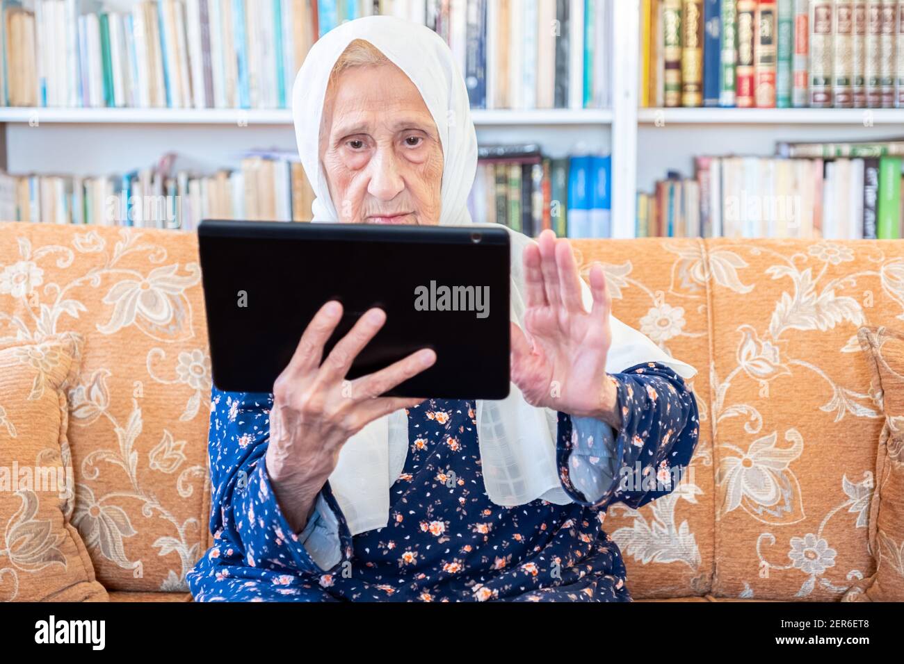 Happy old arabic muslim woamn using technology while sitting on couch Stock Photo