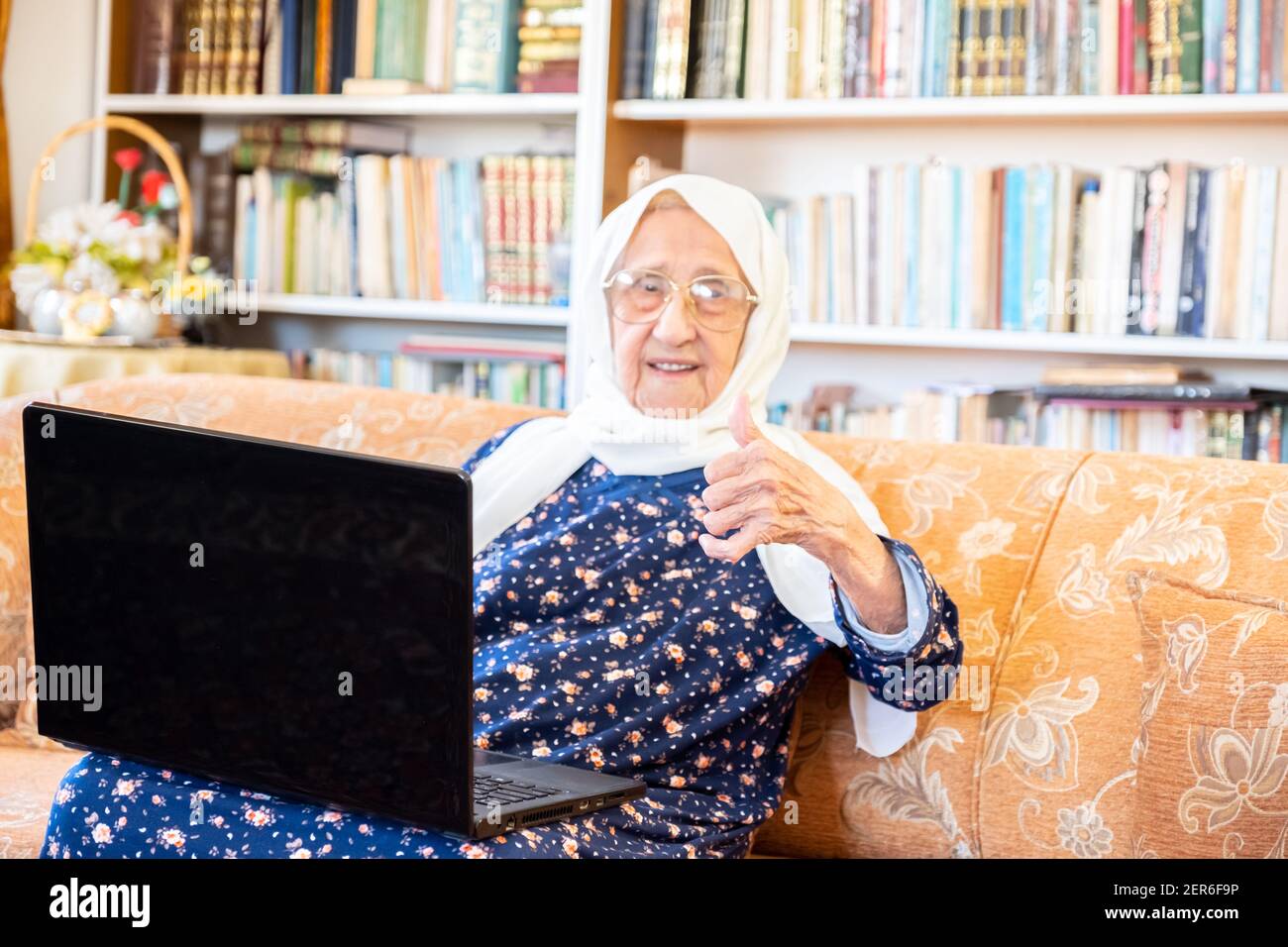Happy old arabic muslim woamn using technology while sitting on couch Stock Photo