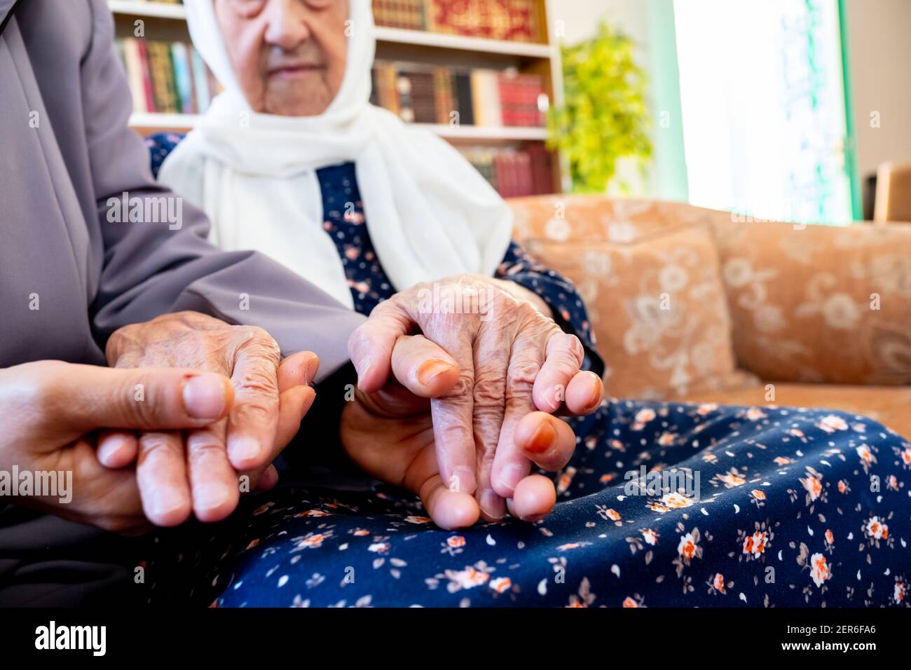 Happy arabic muslim granddaughter holding her grandmother hands Stock