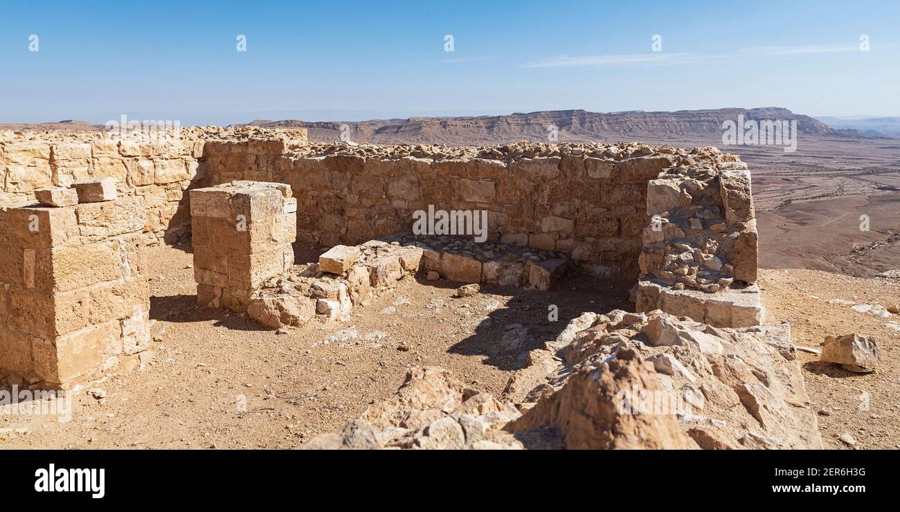 interior stone walls and pillars of the ancient Nabatean Makhmal Fortress on the rim of the Maktesh Ramon crater in Israel with Mount Ardon and a hazy Stock Photo
