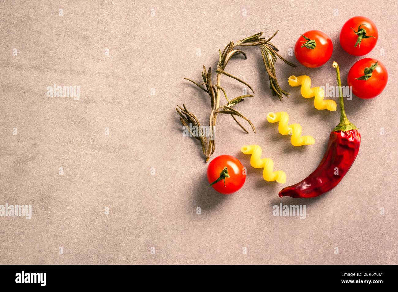 Ripe tomatoes, rosemary, corkscrew pasta and a dried red chilli pepper arranged on a countertop Stock Photo