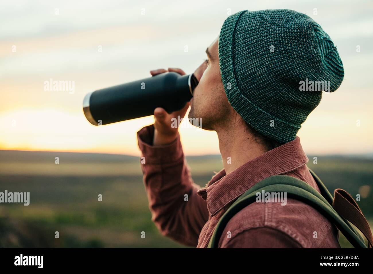 Caucasian male adventurer wearing beanie hiking in mountain quenching thirst drinking water  Stock Photo