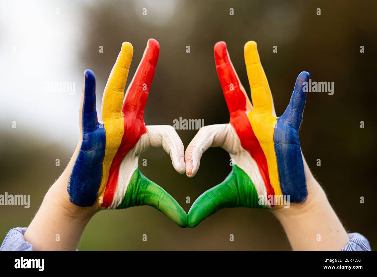 Kid hands painted in Seychelles flag color show symbol of heart and love gesture on nature background Stock Photo