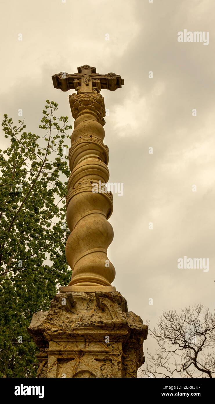 Historic catholic cross, a monument spiraling to sky with Jesus on the cross scene on top. This statue is placed in front of the old hospital de la sa Stock Photo