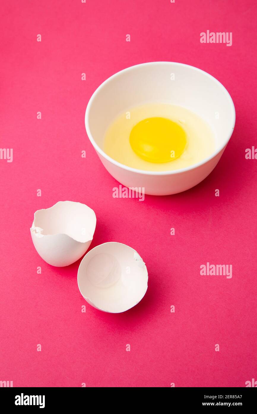 Broken egg in bowl near shell on pink surface Stock Photo