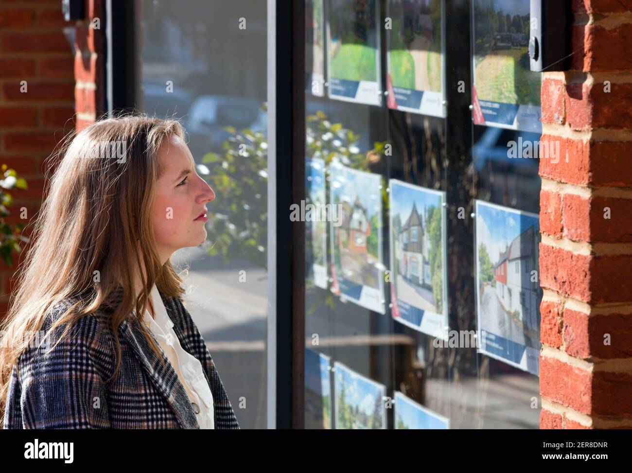 A young woman ( model released ) looking in an estate agent window in Surrey, England, Uk. February 2021 Stock Photo