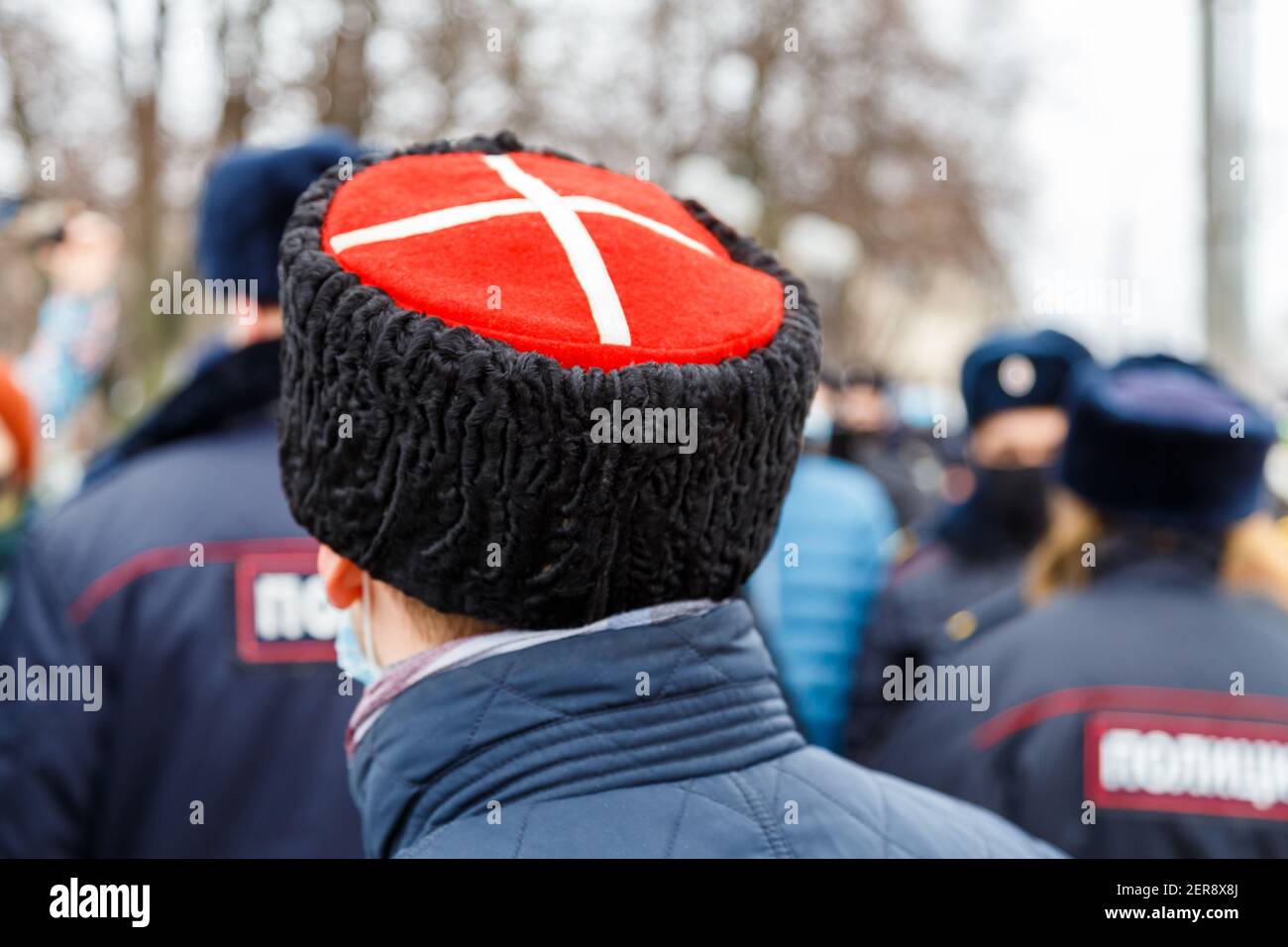 man in cossack hat with white cross on red watching blurry crowd of people - view from back. Stock Photo