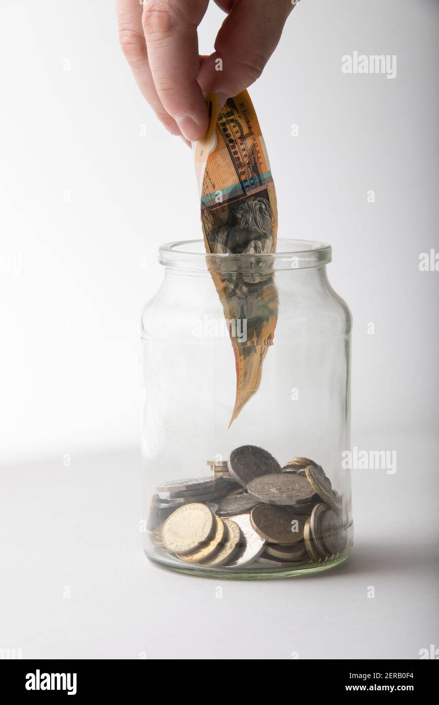 Male hand placing Australian 50 dollar note in coin jar. Stock Photo