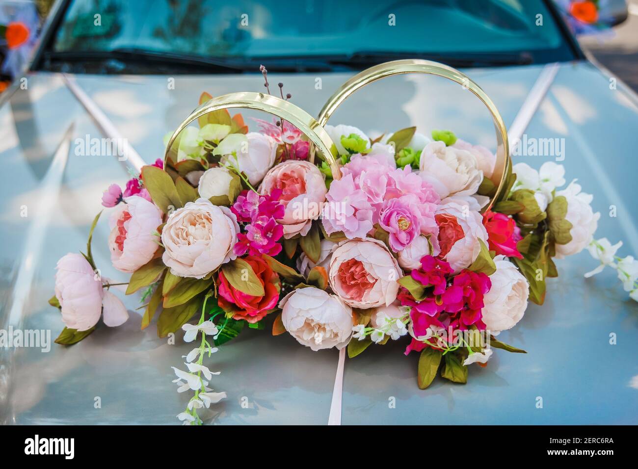 Decoration of artificial flowers of roses and wedding rings on the hood of the car close-up. Stock Photo