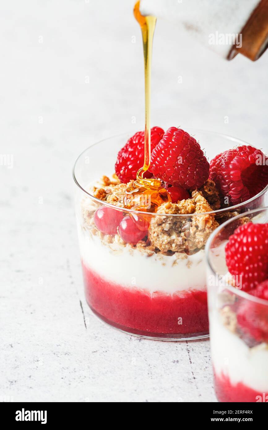Honey pour on a yogurt parfait with home made granola, raspberry puree and fresh raspberries and cranberries. Stock Photo