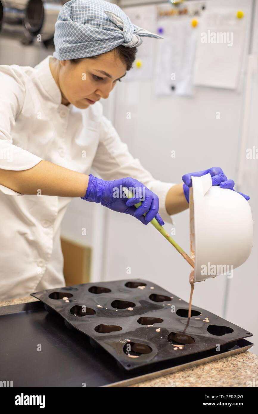 Woman confectioner pouring liquid chocolate into rubber mold tray for