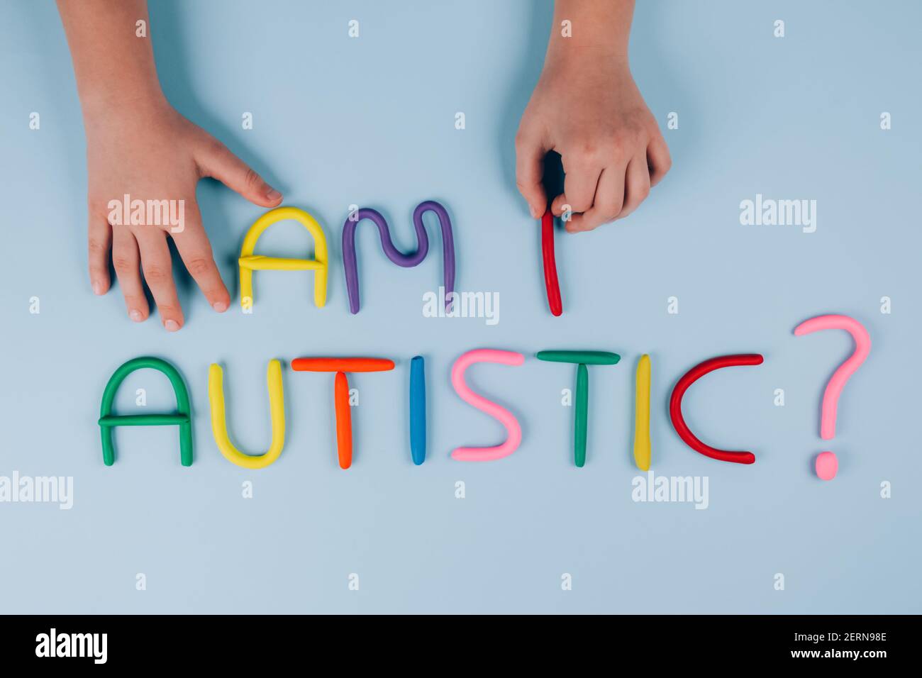 World Autism Awareness Day concept, symptoms - multicolored letters, Am I Autistic - on light blue background with child hand. Autism spectrum Stock Photo