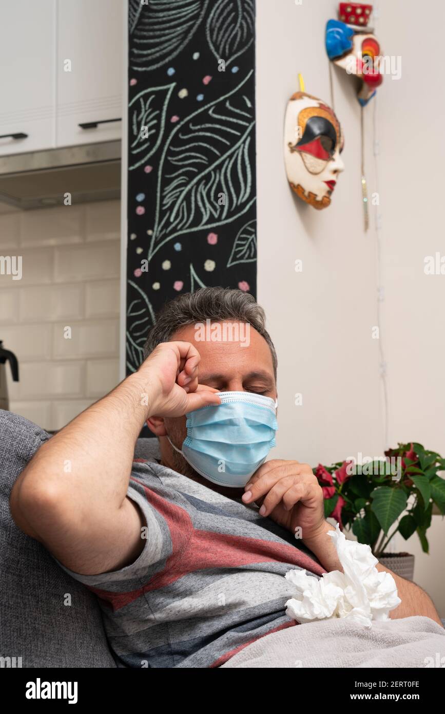 Adult man feeling unwell with sars covid influenza virus infection symptoms arranging disposable medical or surgical mask covering mouth and nose to p Stock Photo