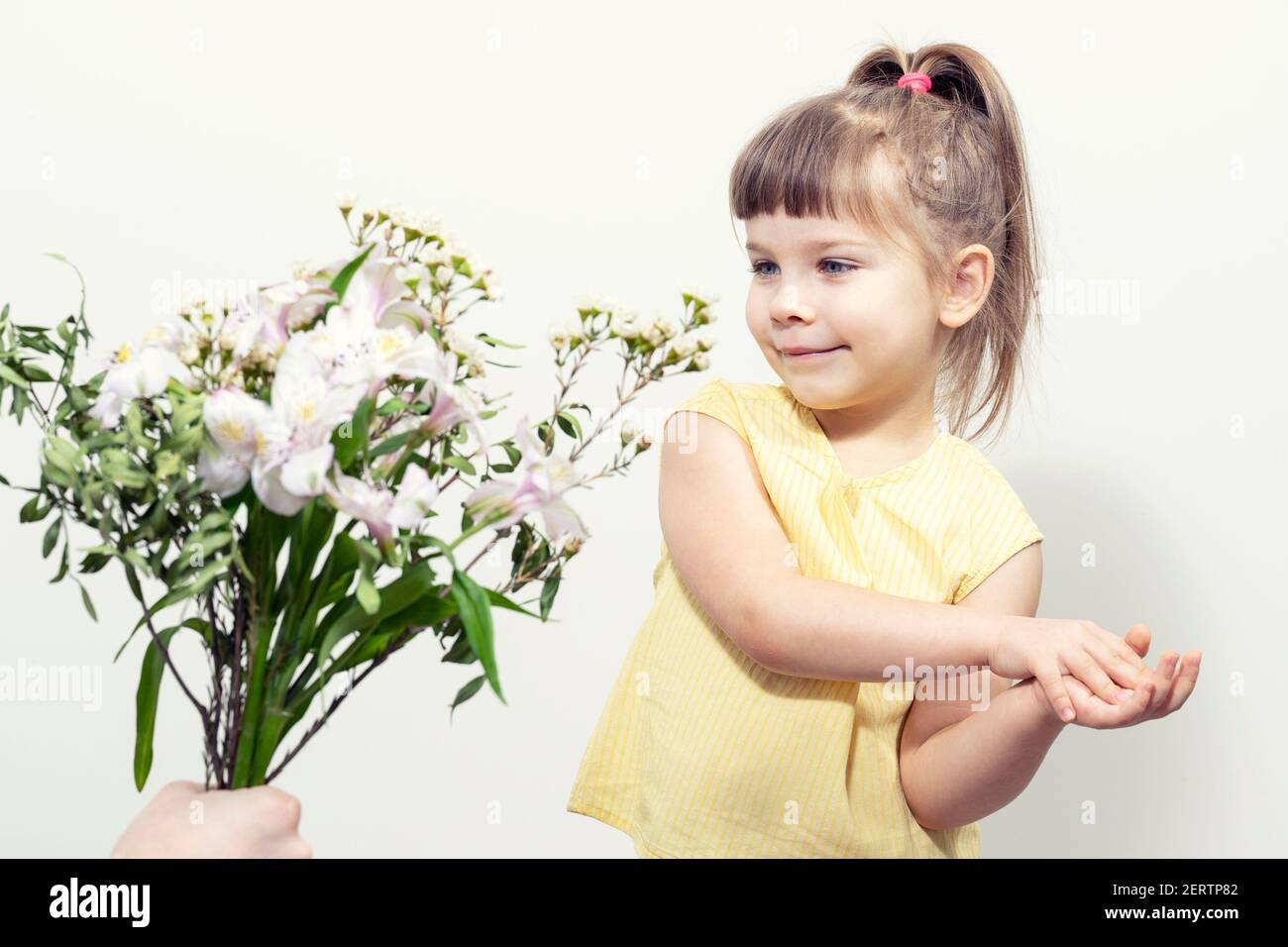 a man's hand holds out a bouquet of white flowers to a cute little girl Stock Photo