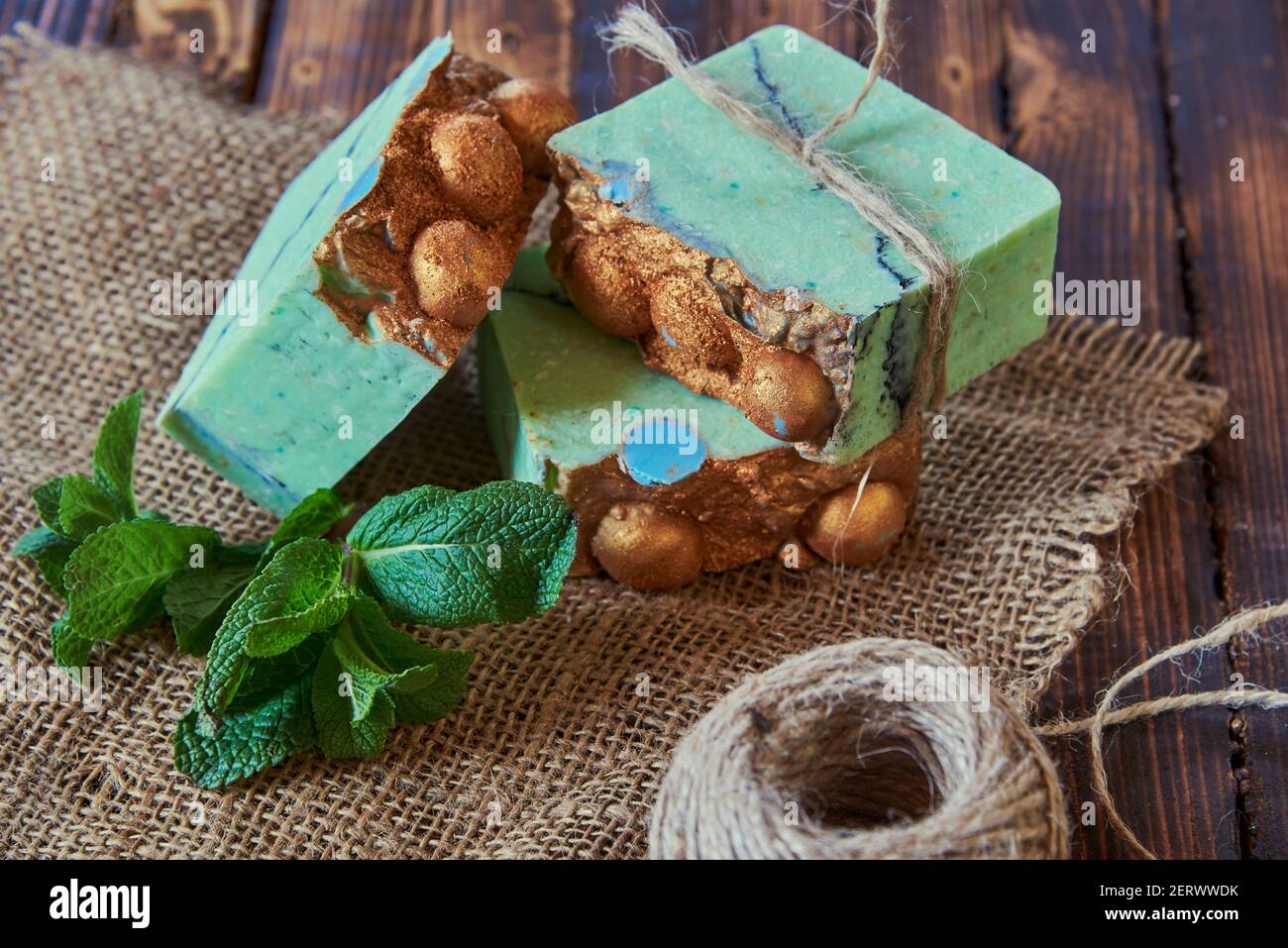 A fragrant green organic handmade soap decorated with mint leaves, burlap and coarse threads on a brown wooden countertop. Stock Photo