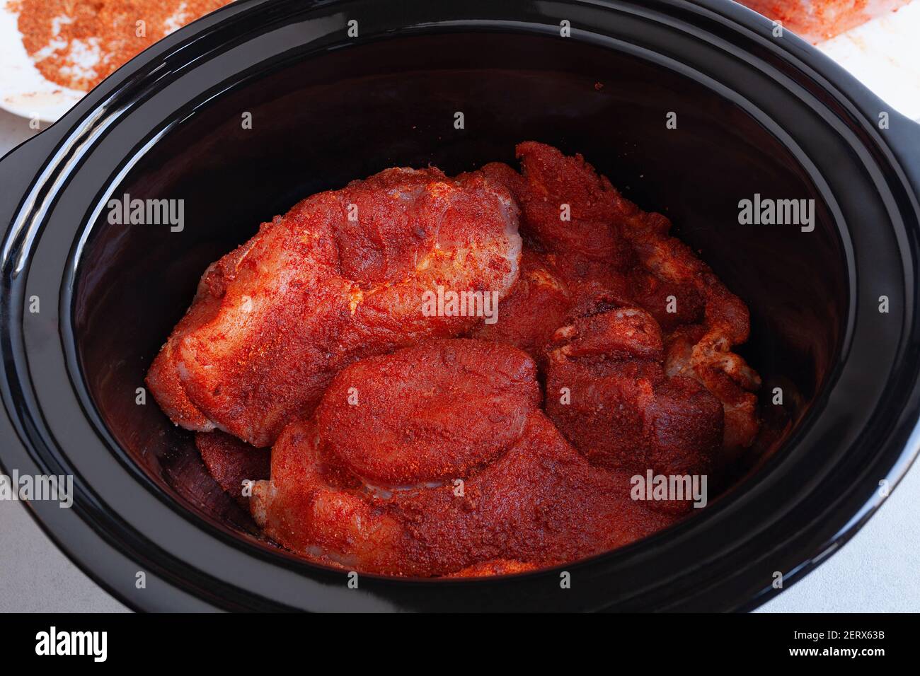 Raw meat covered in spices and dry rub, ready for cooking in slow cooker, placed in black clay