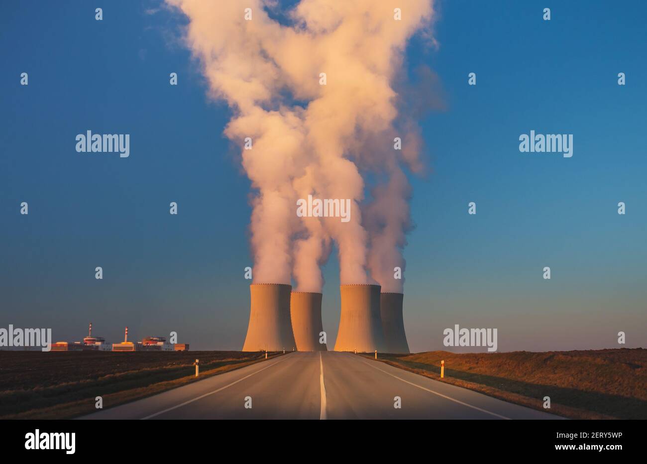 Temelin, Czech republic - 02 28 2021: Nuclear Power Plant, Steaming cooling towers in the landscape at sunset, road leading to factory in foreground Stock Photo