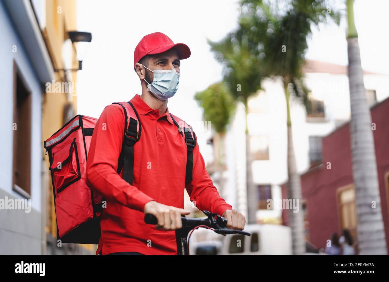 Rider man delivering meal with electric scooter in the city while wearing face mask during corona virus outbreak Stock Photo