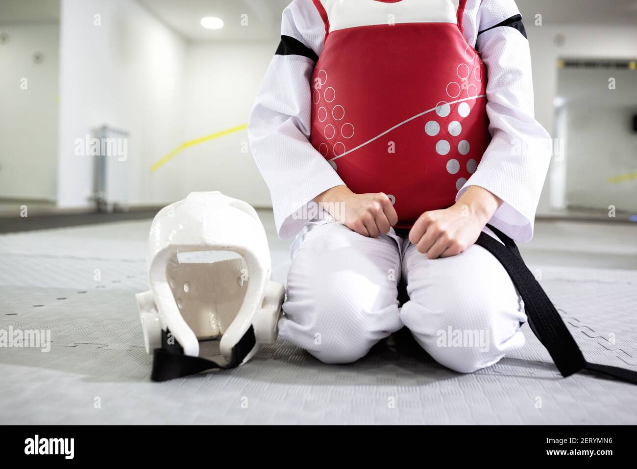 Martial artist in protective gear sitting down and holding a helmet