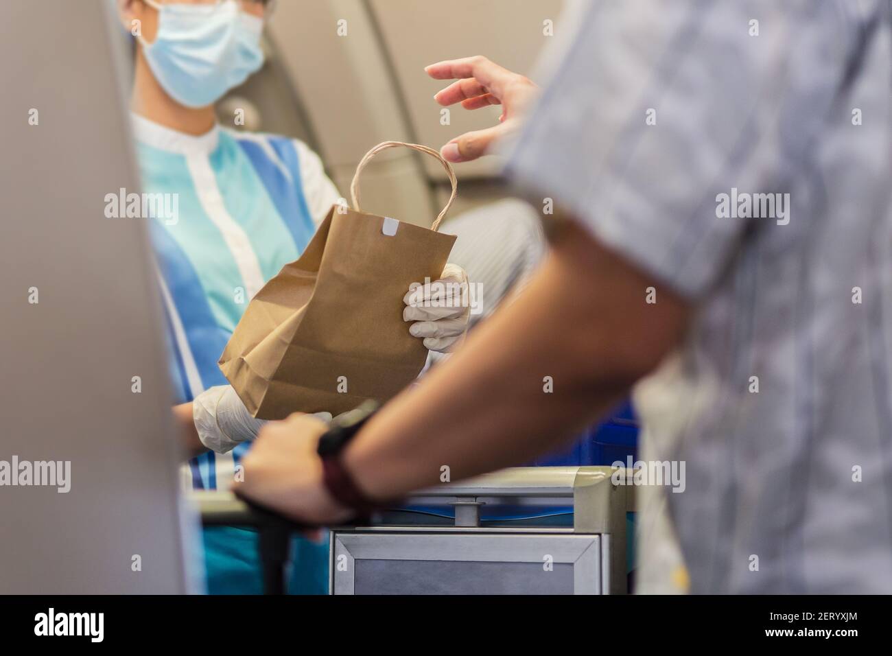 Flight attendant in face mask with gloves giving meals to the passenger travel bubble. Stock Photo