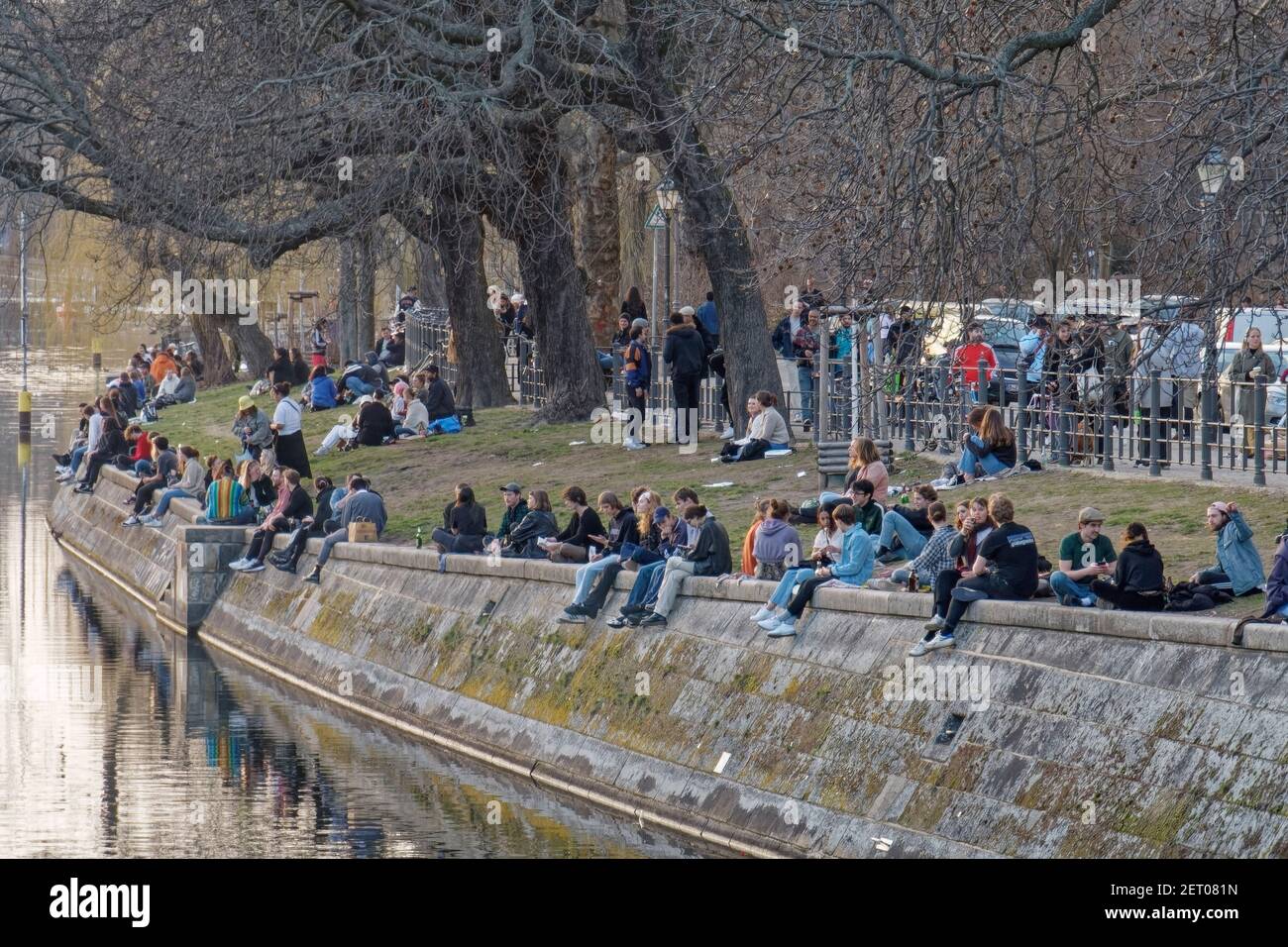 Junge Leute sitzen am Landwehrkanal in Kreuzberg, Urbanhafen, Berlin, Vorfruehling, Lockdown, AHA-Regeln, Stock Photo