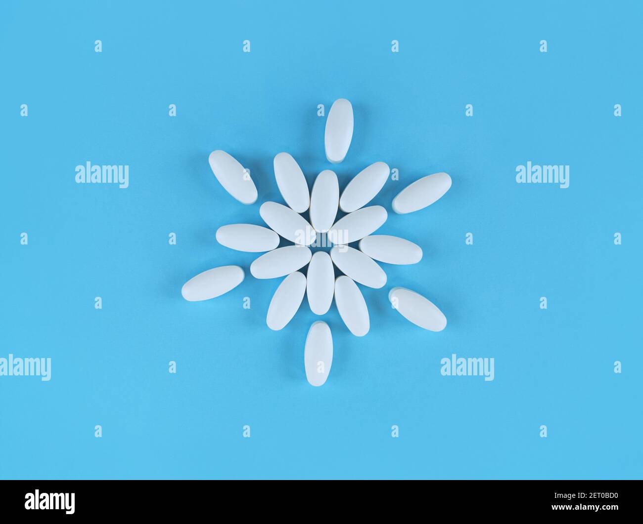 Flower shape made from white tablets on blue backdrop. Stock Photo