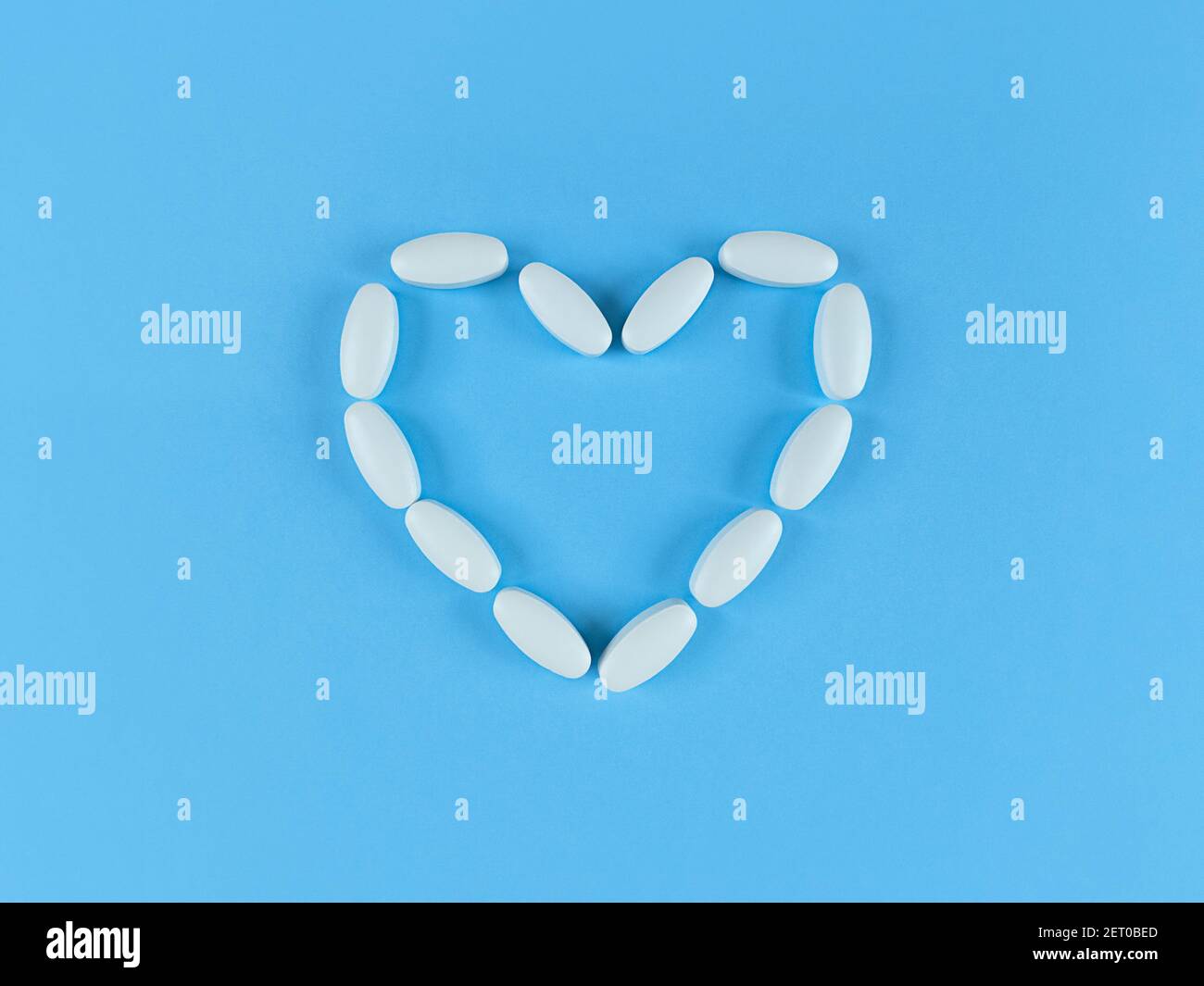 Heart shape made from white tablets on blue backdrop. Stock Photo