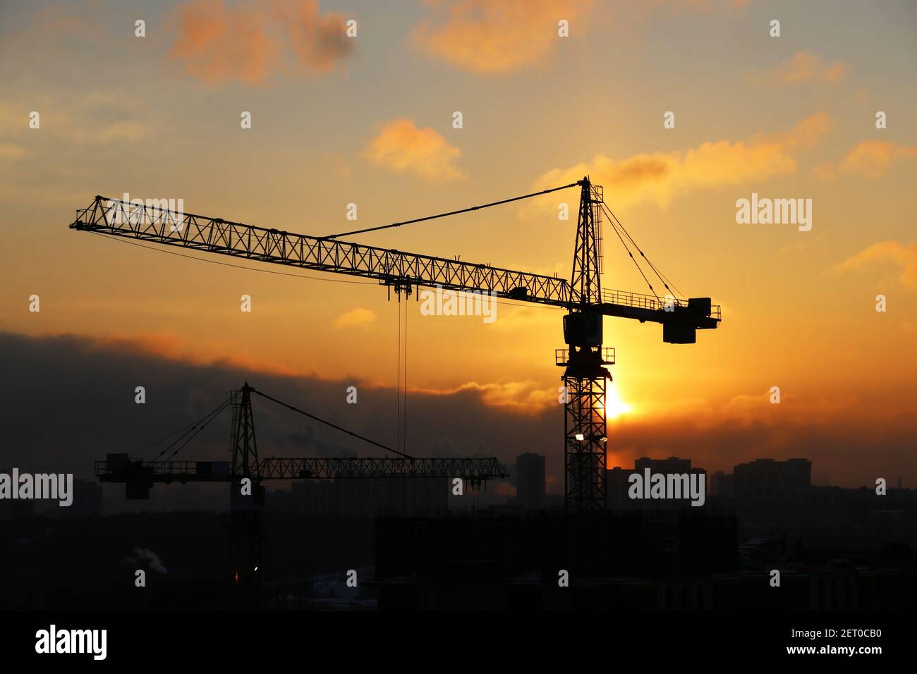 Silhouettes of construction cranes and unfinished residential buildings on sunrise sky and smoke background. Housing construction, apartment block Stock Photo
