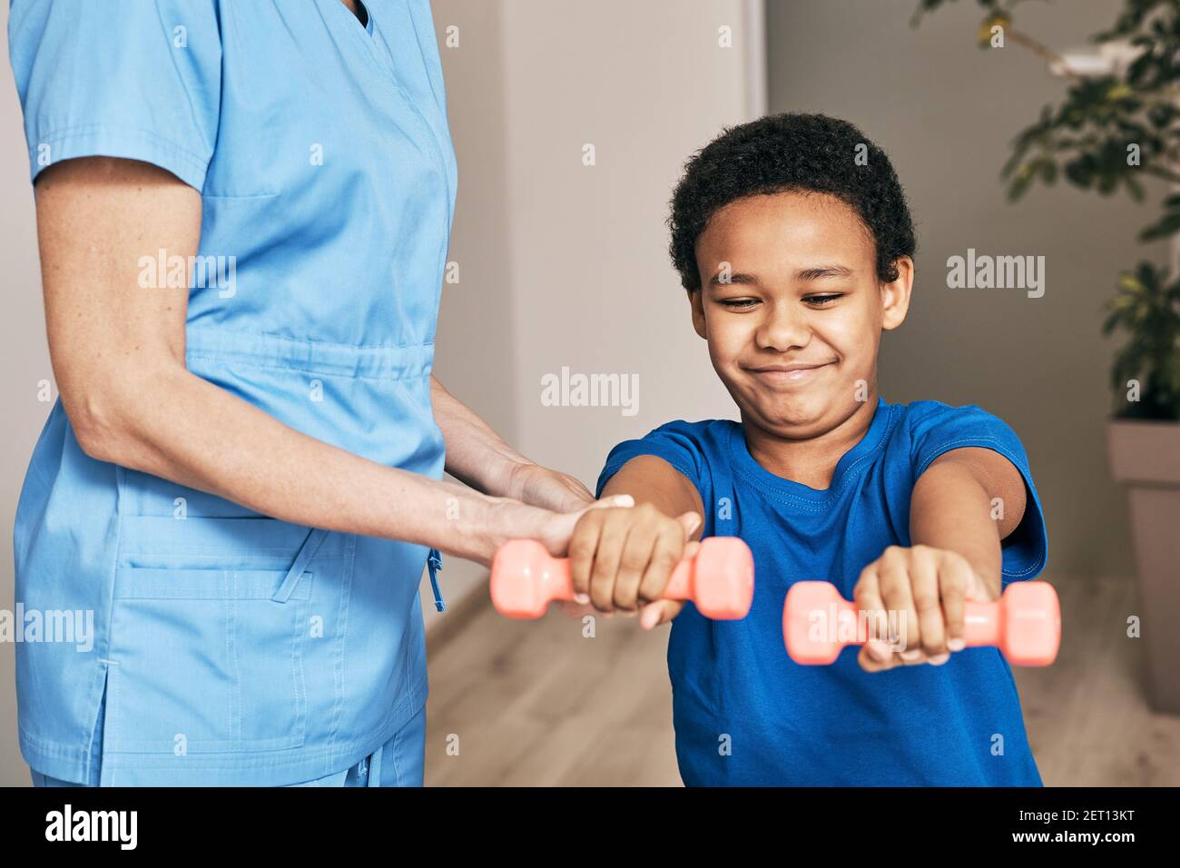 African American boy trains with physiotherapist using dumbbells at rehab center Stock Photo