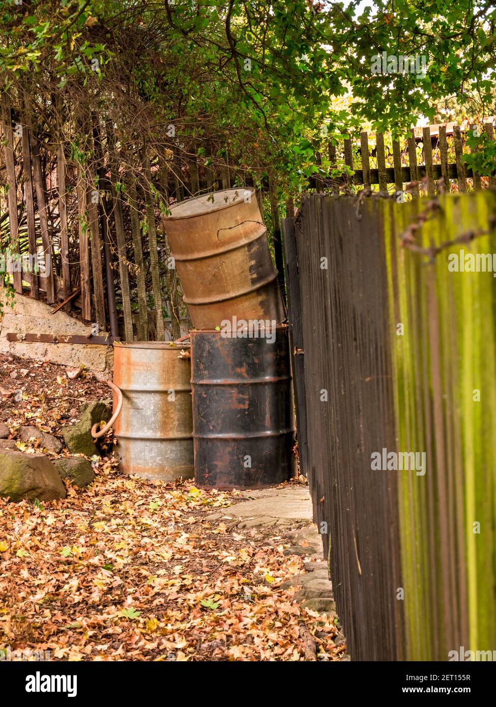 Old metal rusty barrels in the corner of a garden at a wooden fence Stock Photo