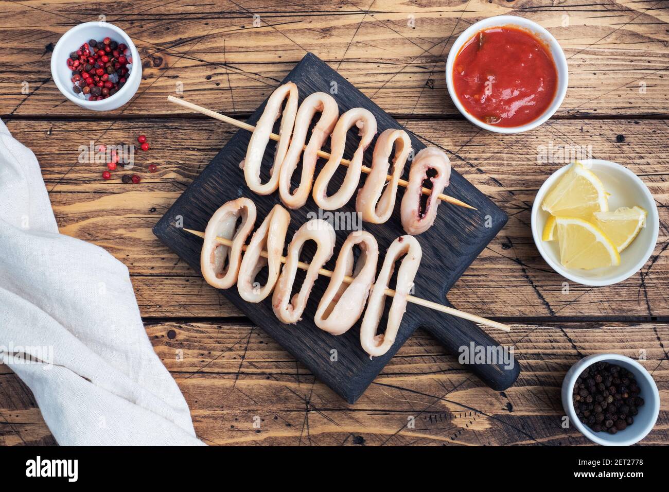 Fried squid rings on a skewer with tomato sauce and lemon. Dark wooden background copy space. Top view Stock Photo