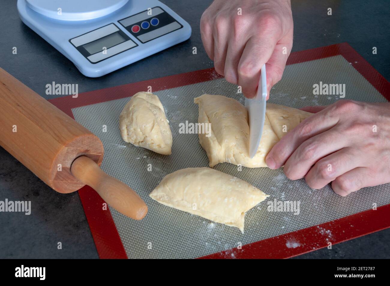 Rolling pin, a flexible plastic cutter, weighing machine. Hands cutting the dough. Stock Photo