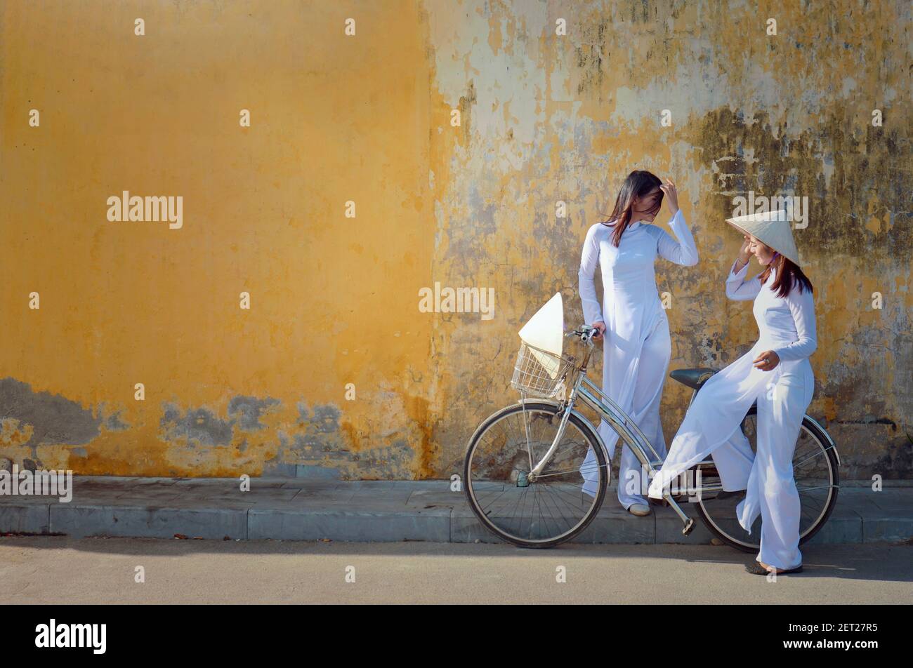 Two beautiful Asian women standing in street talking, Hoi An, Vietnam Stock Photo