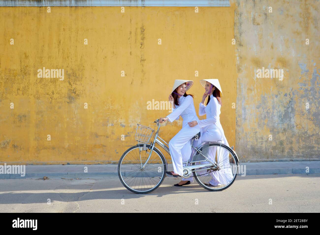 Two beautiful Asian women riding a bicycle in the city, Hoi An, Vietnam Stock Photo