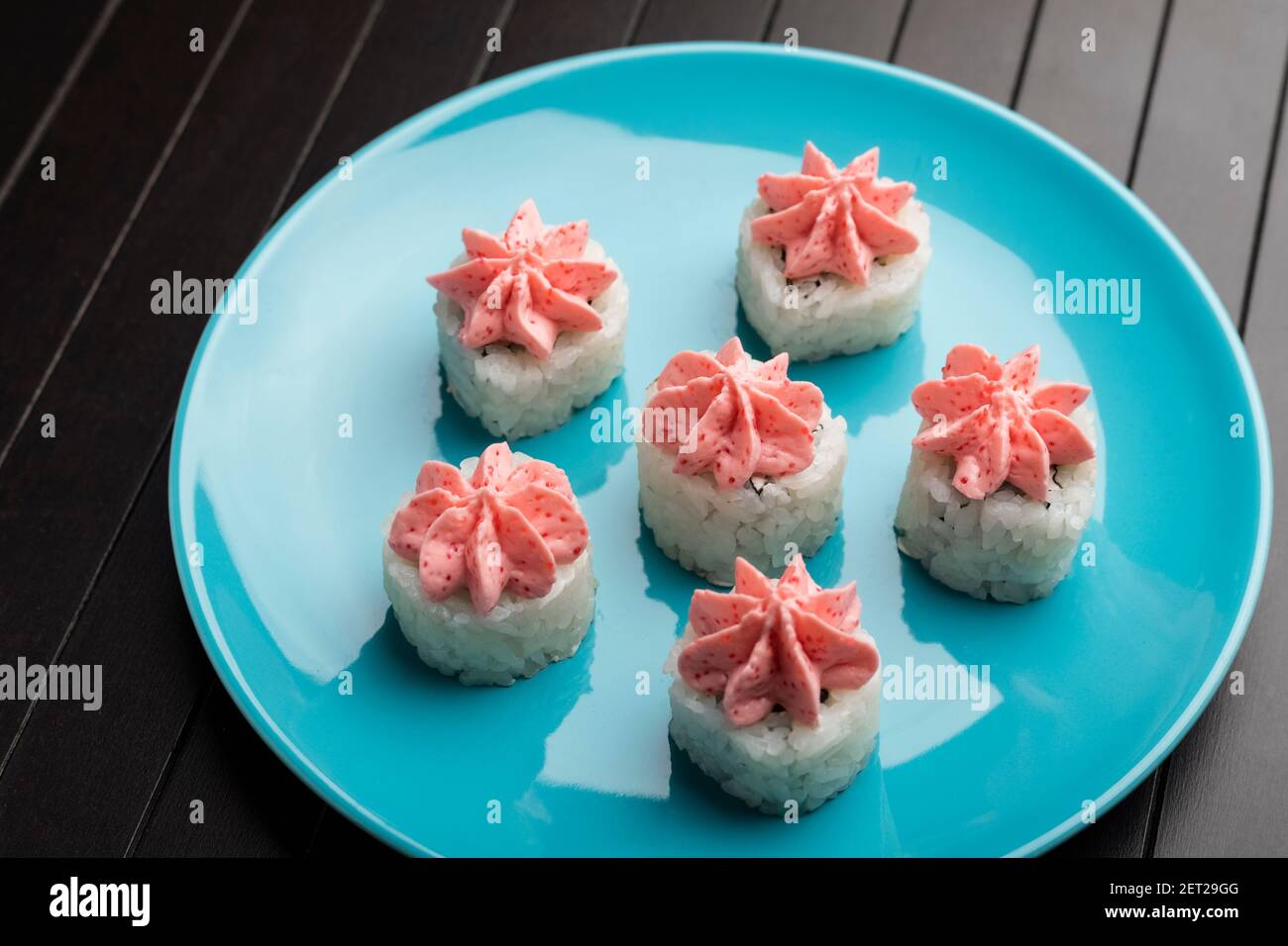 rolls with pink lava sauce on a blue plate, on a wooden table. Serving Japanese food Stock Photo
