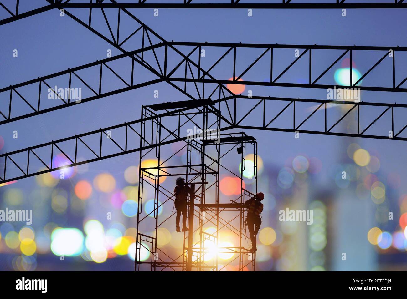 Silhouette of two construction workers climbing scaffolding at night, Thailand Stock Photo