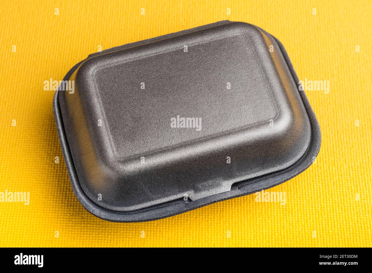 Black closed styrofoam box on yellow background Stock Photo