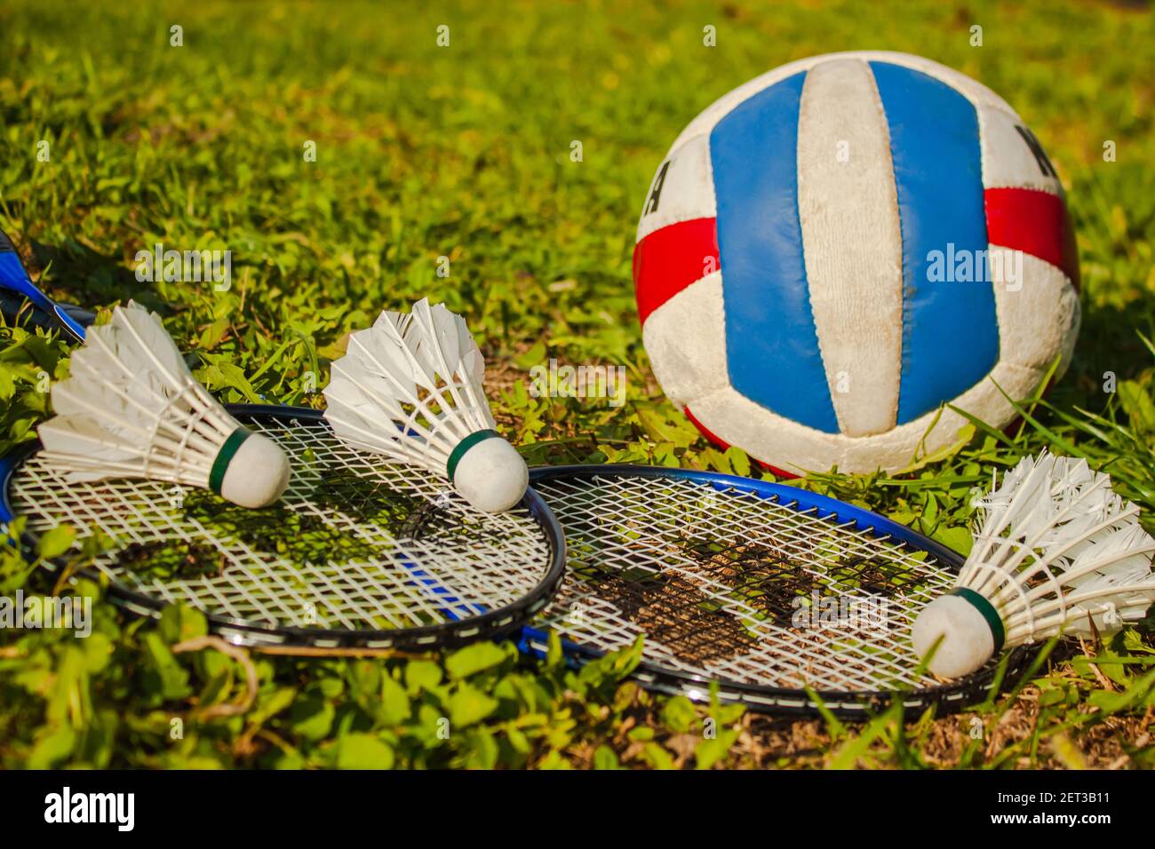 Three shuttlecocks, two badminton rackets and a volleyball ball on the ...