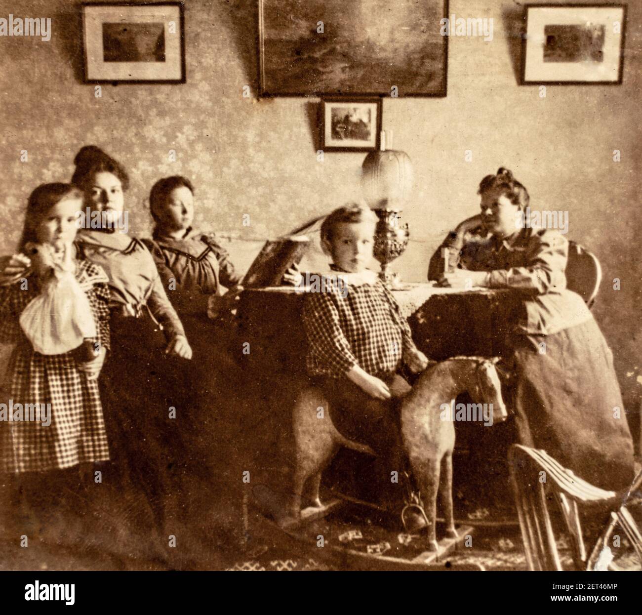 Russia - CIRCA 1900s: Group portrait shot of tree female and two children in dinning room. Boy playing on wooden rocking horse. Vintage Carte de Viste Stock Photo